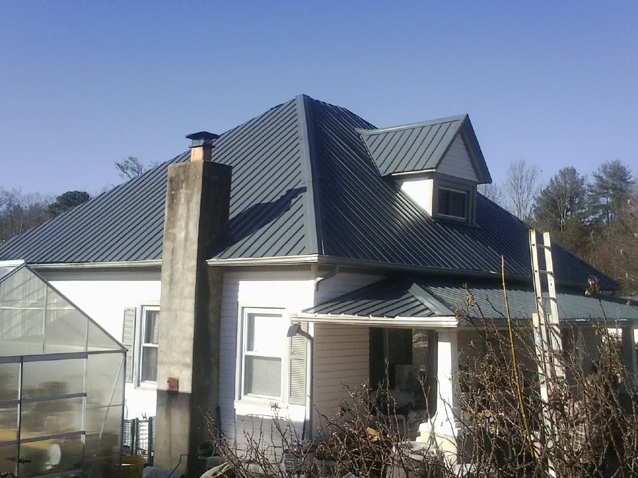 Dark blue standing seam metal roof on a white farmhouse with dormer — Slate & Tile Roof Repair by Roofing Brothers in Holmen