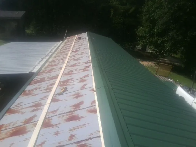 Old rusted panels beside newly installed green metal roofing — Wind Damage Roof Repair by Roofing Brothers in Holmen