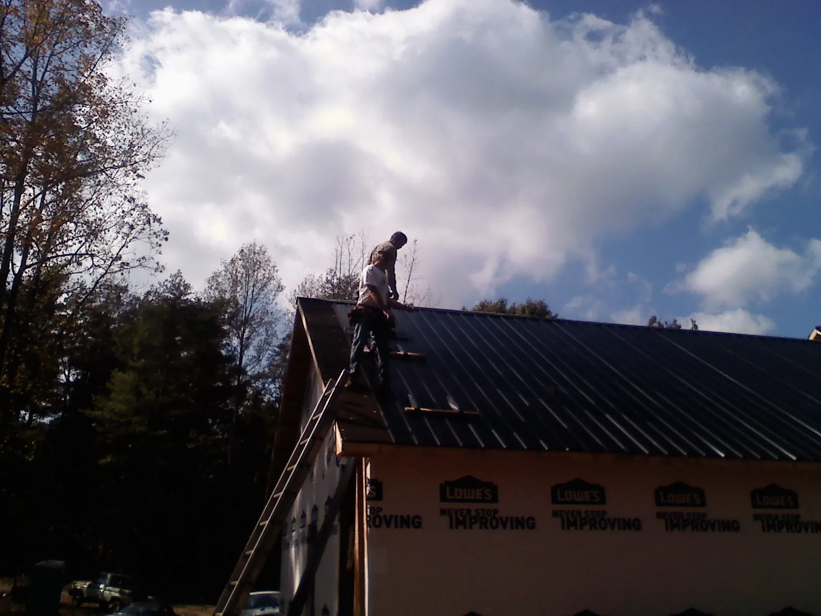 Roofer fastening dark metal panels high against a cloudy sky, from a Roof Inspection job in Holmen
