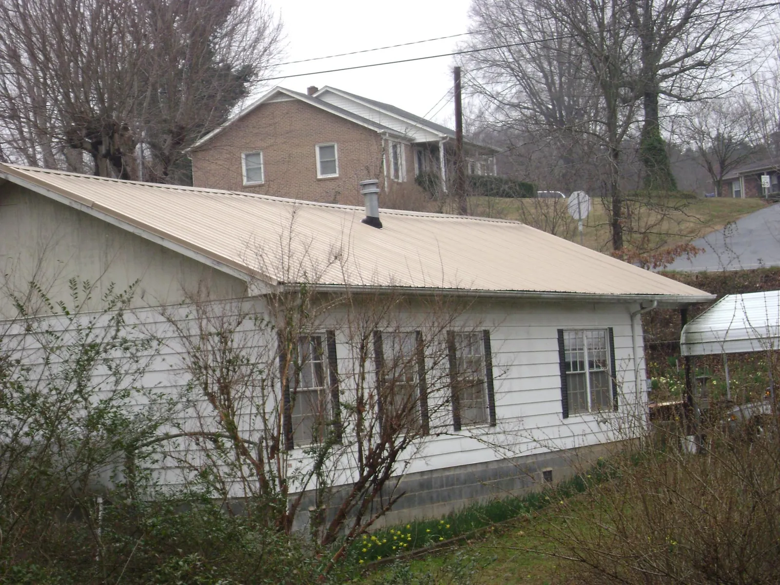Tan metal roof on a white sided house set into a hillside — Commercial Roofing by Roofing Brothers in Holmen