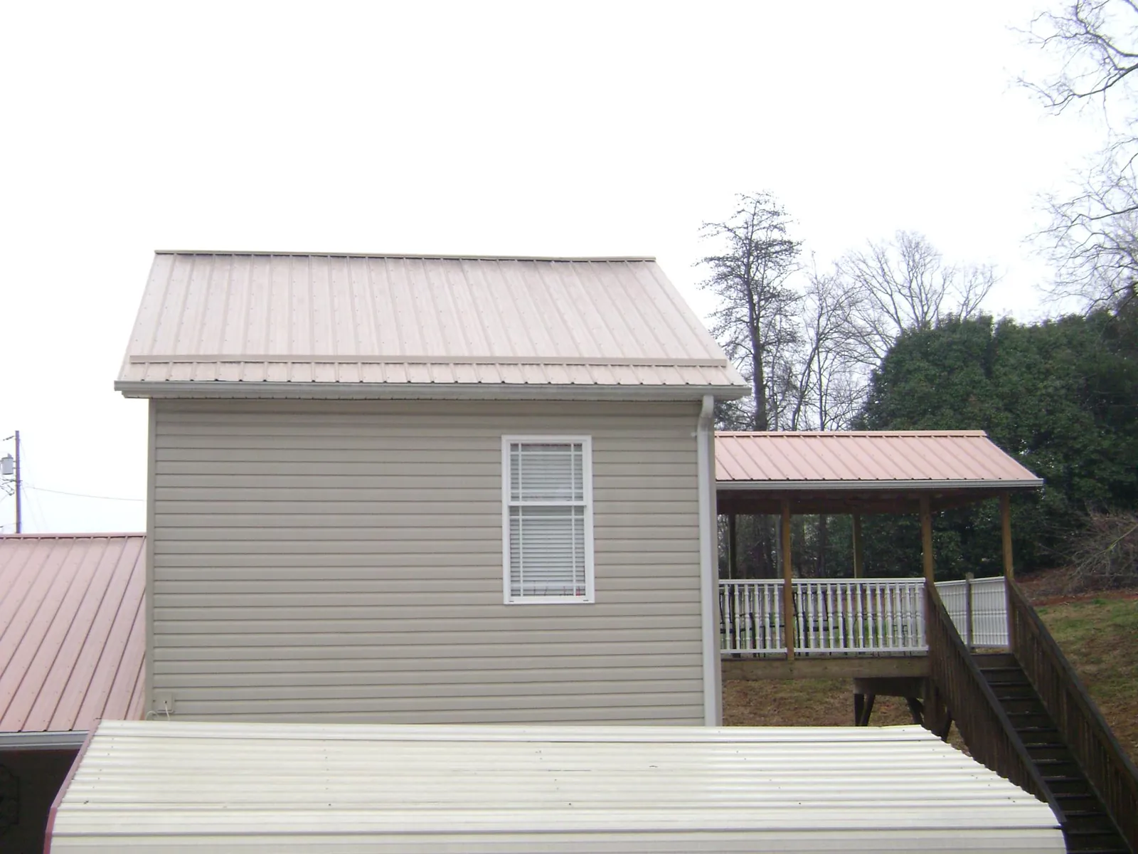 Tan metal roofs on a two story addition and attached porch, from a Roof Replacement job in Holmen